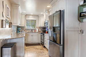 Kitchen featuring white cabinetry, sink, light stone counters, and appliances with stainless steel finishes