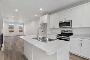 Kitchen featuring wood-type flooring, sink, an island with sink, white cabinetry, and stainless steel appliances