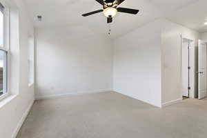 Carpeted empty room featuring vaulted ceiling, a wealth of natural light, and ceiling fan