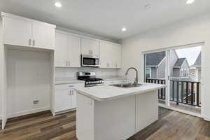 Kitchen featuring white cabinetry, sink, appliances with stainless steel finishes, and an island with sink