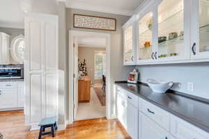 Bar featuring white cabinets, light hardwood / wood-style floors, and crown molding