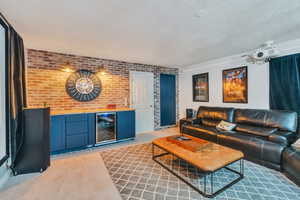 Living room with wine cooler, brick wall, bar area, and a textured ceiling