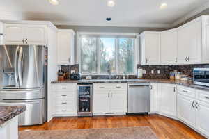 Kitchen featuring white cabinets, stainless steel appliances, light hardwood / wood-style floors, and beverage cooler