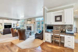 Living room with a fireplace, light hardwood / wood-style floors, built in desk, and crown molding