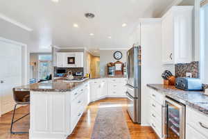 Kitchen featuring a kitchen bar, beverage cooler, white cabinets, light wood-type flooring, and appliances with stainless steel finishes