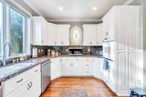 Kitchen featuring dark stone countertops, white cabinetry, ornamental molding, and light hardwood / wood-style floors