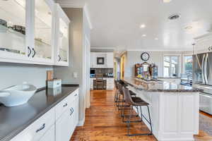 Kitchen with ornamental molding, white cabinetry, appliances with stainless steel finishes, a kitchen breakfast bar, and dark wood-type flooring