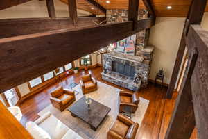 Living room with wood ceiling, wood-type flooring, high vaulted ceiling, beamed ceiling, and a stone fireplace