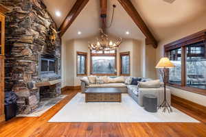 Living room with hardwood / wood-style floors, an inviting chandelier, a stone fireplace, and beam ceiling