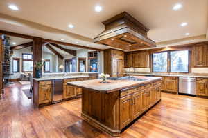 Kitchen with custom range hood, sink, an island with sink, stainless steel dishwasher, and light hardwood / wood-style floors