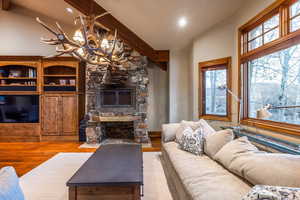 Living room with beam ceiling, a wood stove, an inviting chandelier, high vaulted ceiling, and light hardwood / wood-style floors