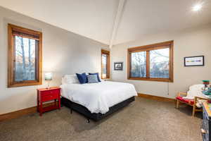 Carpeted bedroom featuring vaulted ceiling with beams and multiple windows