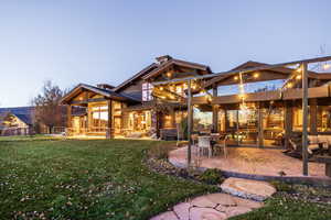 Back house at dusk featuring a lawn, a patio area, and a balcony