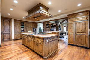 Kitchen with wood counters, an inviting chandelier, premium range hood, a center island with sink, and light wood-type flooring