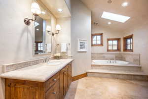 Bathroom with vanity, tiled bath, and vaulted ceiling with skylight