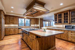 Kitchen featuring light hardwood / wood-style flooring, premium range hood, sink, a kitchen island with sink, and wooden counters