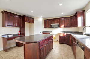 Kitchen featuring light tile patterned flooring, appliances with stainless steel finishes, a kitchen island, and sink