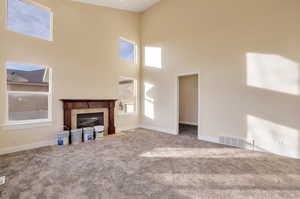 Unfurnished living room featuring a towering ceiling, carpet floors, and a tile fireplace