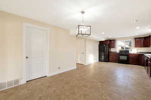 Kitchen with dark brown cabinetry, hanging light fixtures, a notable chandelier, light tile patterned floors, and black appliances