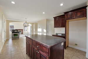 Kitchen with light tile patterned floors, decorative light fixtures, stainless steel range oven, a chandelier, and a kitchen island