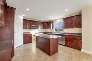 Kitchen with light tile patterned flooring, a center island, stainless steel appliances, and sink