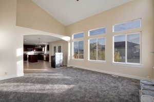 Unfurnished living room featuring carpet floors and high vaulted ceiling