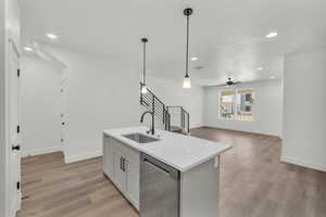 Kitchen with light wood-type flooring, stainless steel dishwasher, sink, decorative light fixtures, and a center island with sink