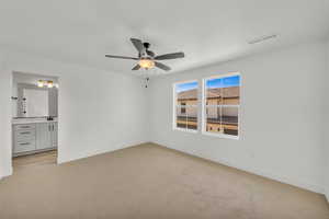 Unfurnished bedroom featuring light carpet, ensuite bath, and ceiling fan