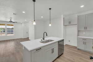 Kitchen with sink, a center island with sink, hanging light fixtures, stainless steel dishwasher, and light wood-type flooring