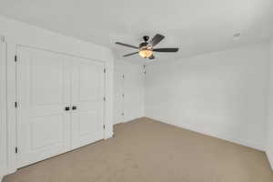 Unfurnished bedroom featuring ceiling fan, a closet, and light carpet