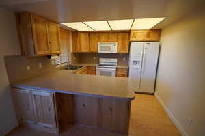 Kitchen featuring decorative backsplash, kitchen peninsula, light wood-type flooring, white appliances, and sink