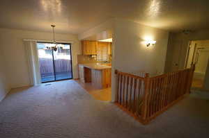 Kitchen featuring light colored carpet, hanging light fixtures, a textured ceiling, and an inviting chandelier