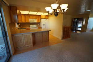 Kitchen featuring kitchen peninsula, tasteful backsplash, white appliances, pendant lighting, and a chandelier