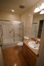 Full bathroom with wood-type flooring, a textured ceiling, toilet, shower / bath combination with glass door, and vanity