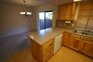 Kitchen with kitchen peninsula, light wood-type flooring, white dishwasher, an inviting chandelier, and hanging light fixtures