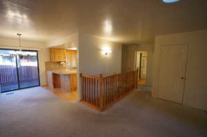 Kitchen featuring hanging light fixtures, light brown cabinetry, light colored carpet, and a textured ceiling