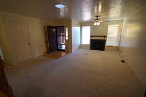 Unfurnished living room featuring ceiling fan, carpet, and a textured ceiling