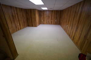 Basement featuring a paneled ceiling, wood walls, and carpet floors