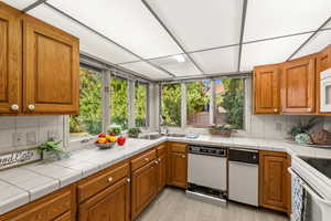 Kitchen featuring tile countertops, decorative backsplash, white appliances, and light hardwood / wood-style flooring