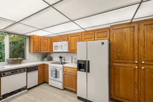 Kitchen with a drop ceiling, white appliances, light hardwood / wood-style flooring, decorative backsplash, and tile counters