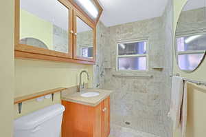 Bathroom with tiled shower, vanity, and toilet