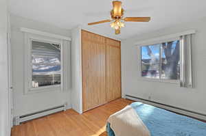 Bedroom with hardwood / wood-style floors, a closet, baseboard heating, and ceiling fan