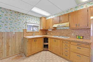 Kitchen with a paneled ceiling, wood walls, white gas cooktop, and sink