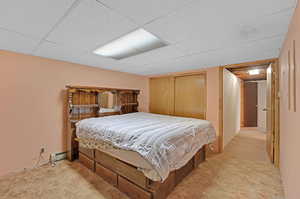 Carpeted bedroom with a closet, a drop ceiling, and a baseboard heating unit