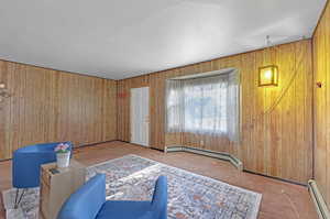 Living area with light colored carpet, baseboard heating, and wood walls