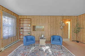 Sitting room featuring carpet flooring, baseboard heating, and wooden walls