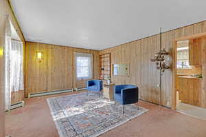 Sitting room with carpet flooring, wooden walls, and a baseboard heating unit