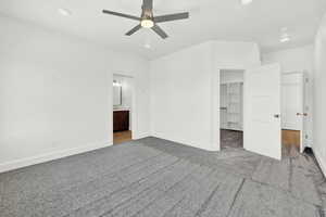 Unfurnished bedroom with ensuite bath, ceiling fan, a walk in closet, a closet, and carpet