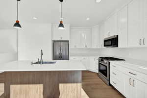 Kitchen with wood-type flooring, stainless steel appliances, white cabinetry, and hanging light fixtures