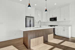 Kitchen featuring pendant lighting, a kitchen island with sink, dark hardwood / wood-style flooring, and stainless steel appliances